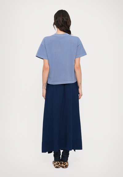 Ανοιχτό μπλε κοντομάνικο crop top συνδυασμένο με μακριά μπλε σκούρα φούστα. Το σύνολο περιλαμβάνει μοτίβο παντόφλες και σχέδιο με πολλαπλές κάλτσες.