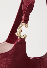 Gros plan sur la sangle texturée en cuir rouge foncé d'un sac à main attachée avec une quincaillerie dorée en forme de "C".