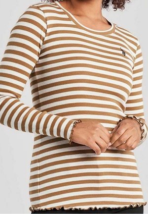 Mujer con una camisa de manga larga acanalada con rayas horizontales blancas y beige, y bordes con volantes en los puños y el dobladillo.