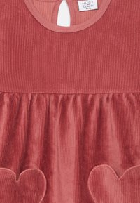 Vestido de pana rojo con textura acanalada, espalda con abertura en forma de ojo de cerradura y aplicaciones en forma de corazón en una falda fruncida.