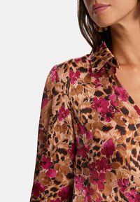 Blouse à col avec un design floral et imprimé léopard dans des teintes de rose, marron et noir. La texture plissée ajoute de la dimension.