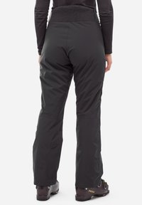 Schwarze isolierte Schneehosen mit strukturiertem Bund, Seitentaschen und verstärkten Säumen, getragen mit schwarzen Skistiefeln mit einem Logo.