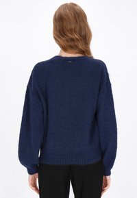 Tengerészeti kék, oversized pulóver puha, texturált anyagból, bordás mandzsettákkal és szegéllyel. A hátsó nyakrészén egy kis logós címke található.