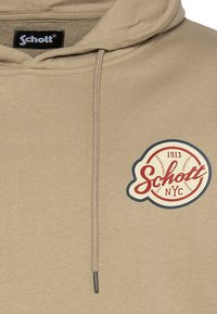 Beżowa bawełniana bluza z kapturem z naszywką z przodu z czerwonymi i granatowymi akcentami. Posiada kaptur ze sznurkiem i ściągacze przy rękawach.