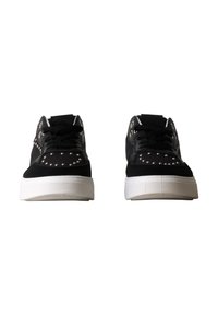 Paire de baskets noires avec des semelles blanches épaisses, des lacets noirs et des détails clous argentés sur la pointe et les côtés, sur fond blanc.