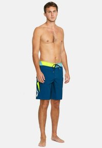 Bañadores para hombre en color azul marino con una cinturilla en amarillo brillante y verde. Presentan un cordón de ajuste, detalle del logo y un diseño aerodinámico.