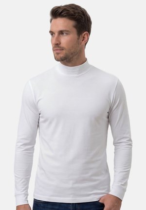 Mand med kort brunt hår iført en tætsiddende hvid langærmet rullekrave, der kigger svagt mod venstre mod en ensfarvet baggrund.