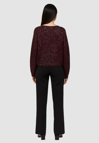 Maglione bordò con un design testurizzato e scintillante, abbinato a pantaloni neri a gamba dritta. L'outfit presenta una vestibilità comoda e maniche lunghe.