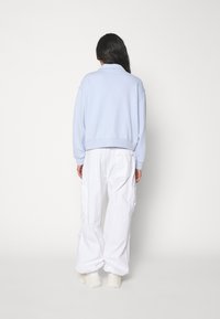Ljusblå sweatshirt med hög krage och ribbat nederkant, i kombination med löst sittande vita cargobyxor. Båda i mjukt material.