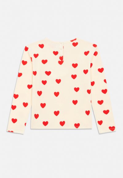 Μπλούζα εκρού με μακριά μανίκια, μοτίβο από κόκκινη καρδιά και κουμπιά στο πίσω μέρος του λαιμού, απλωμένη επίπεδη σε λευκό φόντο.