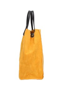 Geel suède tote bag met een gladde textuur, zwarte leren handvatten, een afgeronde bovenkant en een drukknopsluiting aan de opening.