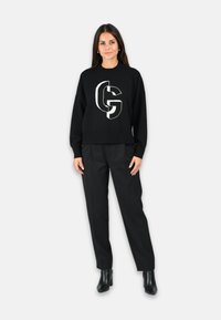 Pull noir avec un grand logo graphique blanc, associé à un pantalon noir et des bottines. Texture lisse, design décontracté.