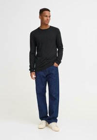 Suéter negro de manga larga con dobladillo acanalado, combinado con jeans azul de corte suelto y zapatillas beige, creando un look casual y en capas.