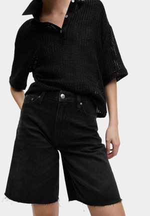 Black, knitted short-sleeve polo top with a collar, paired with high-waisted, black denim shorts featuring frayed hems and button detailing.