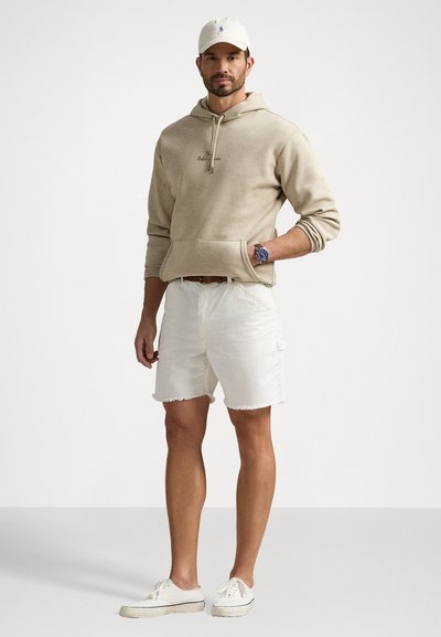 Beige sweatshirt med snøre, forlommer; hvide slidte shorts; hvide sneakers; ur; baseballkasket. Enkel, afslappet outfit.