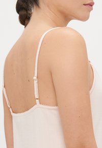 Lys rosa camisol med tynne justerbare stropper, teksturert stoff, blondekant langs halslinjen og gullfargede detaljer på stroppene.