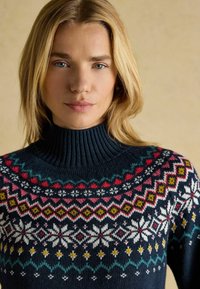 Marineblauer gestrickter Pullover mit hohem, geripptem Kragen. Verziert mit bunten geometrischen Mustern in Pink, Gelb und Weiß über der Brust.