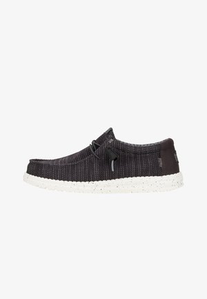 Zapato negro de tejido tipo slip-on con una suela blanca moteada, que presenta cordones elásticos y un collar acolchado para mayor comodidad. Diseño de parte superior texturizada.
