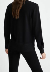 Pull en maille noir à manches longues, avec un col rond et une bande texturée à l'ourlet. Comprend des fentes latérales et une finition lisse.