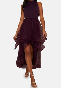 Violetti mekko, jossa on tiukka yläosa ja kerrostettu tüllihame. Korkea-matala helma, jossa on röyhelöreunat, yhdistettynä nauhakuosisilla koroilla.