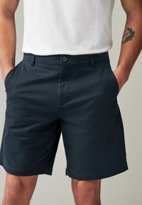 Pantalones cortos de color azul marino oscuro, elaborados en una mezcla de algodón, con un diseño de frente plano, bolsillos laterales, cierre de botón y un ajuste entallado. Textura suave y dobladillo prolijo.