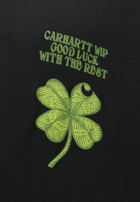 Czarna koszulka z zieloną grafiką czterolistnej koniczyny oraz napisem "Carhartt WIP Powodzenia w dalszej drodze" nad nią.