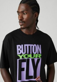 Black cotton t-shirt featuring bold text in purple and green stating "BUTTON YOUR FLY." Includes a small Levi's logo tag. Short sleeves.