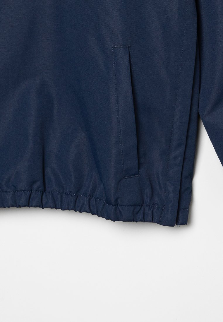 Chaqueta azul marino con bajo elástico, tejido suave y un bolsillo lateral. Diseño sencillo sin hardware ni patrones visibles.