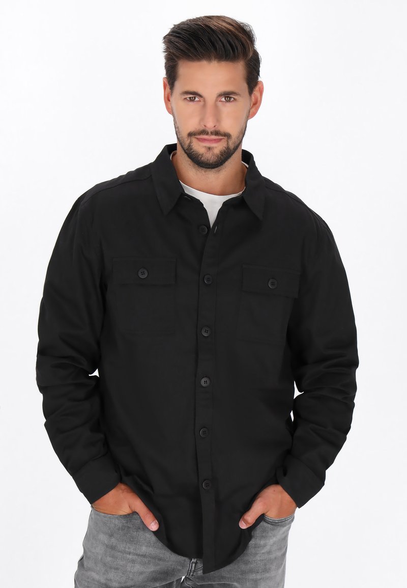 Camicia nera con bottoni, due tasche sul petto, maniche lunghe e colletto. Texture liscia e design aderente.