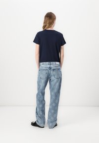 T-shirt navy a maniche corte abbinato a jeans a palazzo azzurri chiari e decorati. Scarpe nere completano l'outfit.