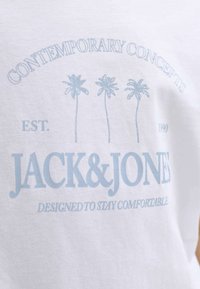 Camisa blanca con texto en azul claro que dice "CONCEPTOS CONTEMPORÁNEOS", tres palmeras, "EST. 1990", "JACK & JONES" y "DISEÑADO PARA MANTENER LA COMODIDAD".