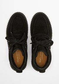 Bottines en suede noires avec des semelles épaisses et texturées. Comprend un bout rond, un design à lacets et des accents métalliques sur les côtés.