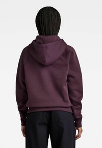 Purple hoodie featuring a textured fabric, a spacious hood, and ribbed cuffs. The back view displays a relaxed fit and minimal detailing.