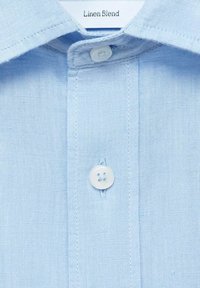 Lichtblauw linnenblend overhemd met een puntige kraag, een enkele witte knoop en zichtbare stikdetails op de knoopsluiting.