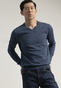 Suéter navy blue con escote en V, hecho de una tela suave, con mangas largas y un dobladillo ajustado, que se combina con jeans de color azul oscuro.