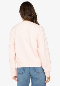 Helles rosa Sweatshirt mit langen Ärmeln, gerippten Bündchen und Saum, in lockerer Passform. Tragend mit blauen Jeans, die einen einfachen, lässigen Stil zeigen.