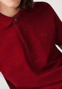 Röd polo-tröja i texturerad tyg med tvåknappsknäppning, korta ärmar och broderad logotyp på bröstet.