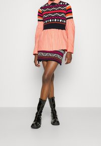 Värikäs pitkähihainen paita, jossa on raidallinen kuvio, ja kuvioitu neulehame. Sisältää mustia, pinkkejä ja oransseja yksityiskohtia. Yhdistetty kiiltäviin mustiin polven korkeisiin saappaisiin.