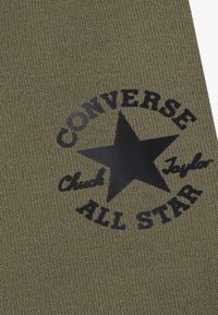 Πλεκτό ύφασμα σε ελιά πράσινο χρώμα με έντονο γραφικό μαύρο αστέρα και την επιγραφή «CONVERSE CHUCK TAYLOR ALL STAR» σε κυκλική διάταξη.