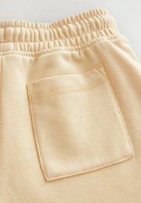 Un pantalon de survêtement couleur crème avec une taille élastique à cordon de serrage, un tissu texturé et une poche arrière cousue de forme rectangulaire.