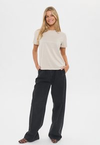 Beige short-sleeve t-shirt, relaxed fit, paired with loose-fitting black denim pants. Footwear features a leopard print pattern.