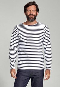Langærmet, hvid bomulds skjorte med marineblå vandrette striber, med en bred udskæring og afslappet pasform. Bæres med mørk denim jeans.