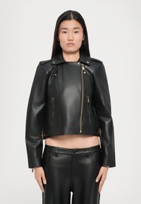 Sort læderjakke med cropped design, guld lynlåse og skulderdetaljer. Har en høj krave og to lynlåslommer foran.