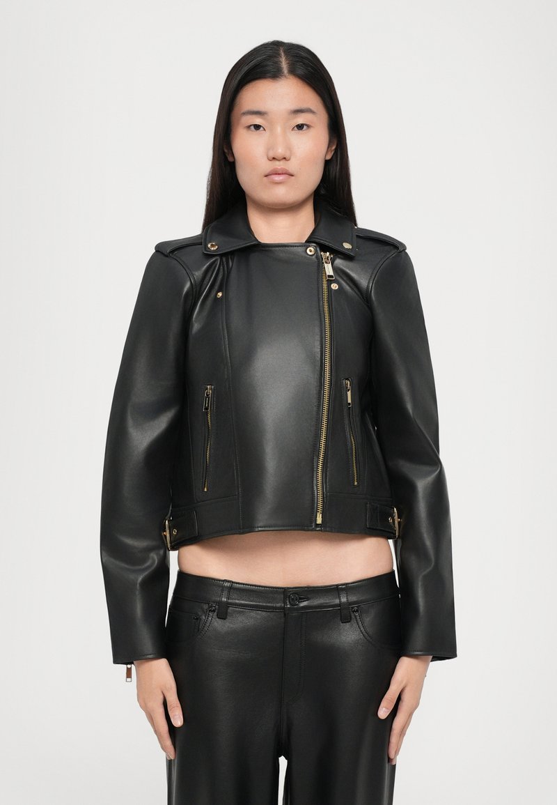 Sort læderjakke med cropped design, guld lynlåse og skulderdetaljer. Har en høj krave og to lynlåslommer foran.