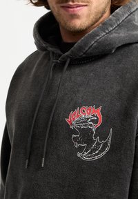 Czarna bluza z kapturem z grafiką smoka i czerwonym napisem "VOLCOM". Wykonana z miękkiego materiału, z kapturem na sznurki i detalem w postaci kieszeni z przodu.