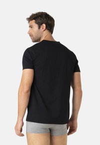 T-shirt noir à manches courtes en coton, avec un col rond, ayant une silhouette ajustée, porté avec un boxer gris.