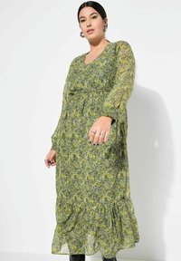 Abito verde lungo con motivo floreale in giallo e bianco, caratterizzato da scollatura a V, maniche voluminose e orlo arricciato. Realizzato in tessuto leggero.