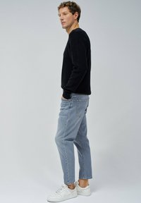 Pull noir côtelé, jean droit bleu clair et baskets blanches. Le mannequin se tient de profil contre un fond neutre.