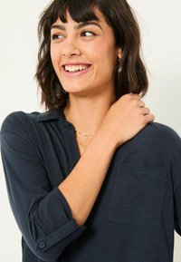 Marineblaues Langarm-Oberteil mit einem Kragen, einer einzelnen Brusttasche und geknöpften Manschetten. Weicher Stoff mit strukturiertem Aussehen.