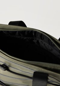 Άποψη από πάνω ενός ανοιχτού σακιδίου πλάτης σε ελιά πράσινο χρώμα με εσωτερική επένδυση μαύρου χρώματος και μαύρη θηλιά χειρολαβής.